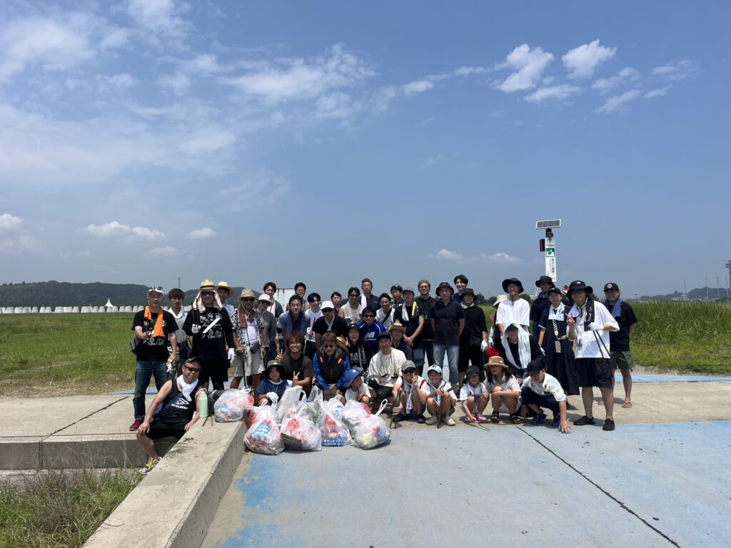 Large group of people posing outdoors with filled trash bags after a community cleanup.