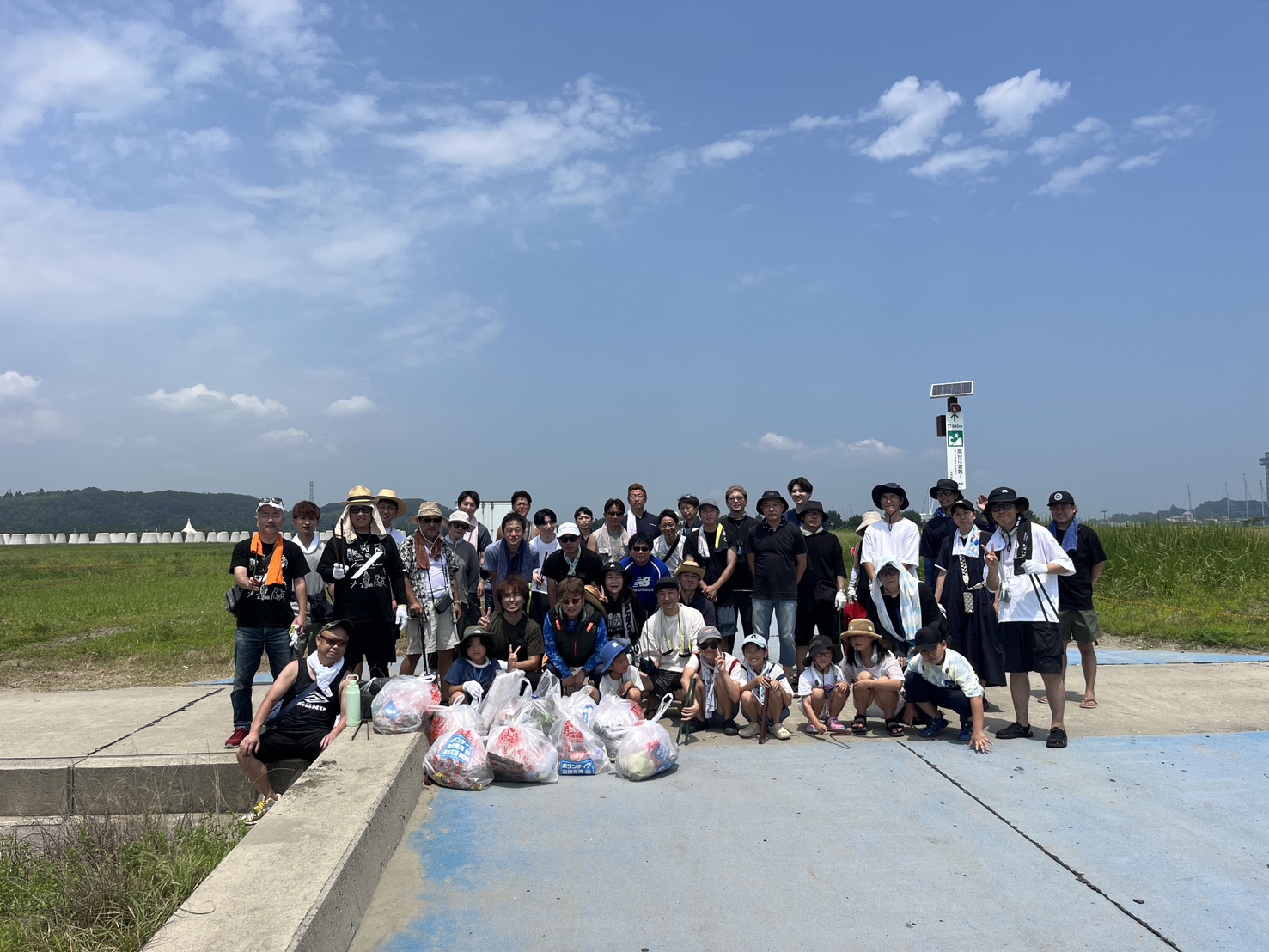 Large group of people posing outdoors with filled trash bags after a community cleanup.