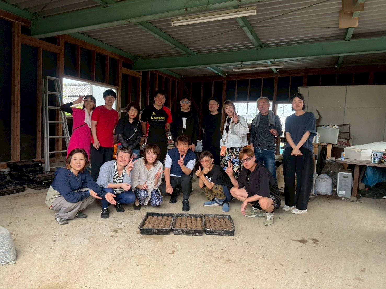 Group of about 18 people posing in a workshop, with trays of seed balls on the floor in front of them.