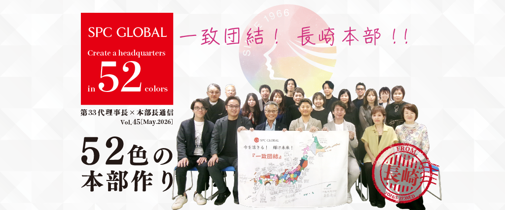 Group of employees posing together with a world map banner, SPC GLOBAL branding on a red square to the left, Japanese slogan overhead.