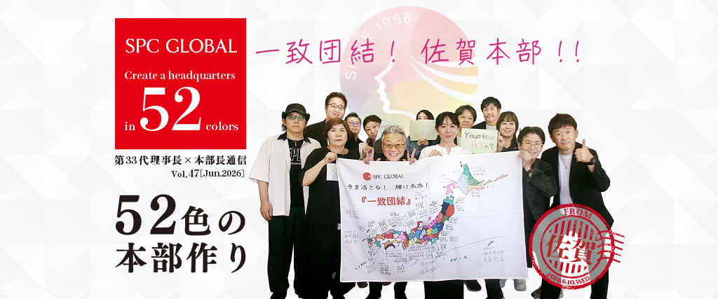 Group of people posing with a large map banner and a red SPC GLOBAL logo, celebrating the '52 colors' headquarters project with Japanese text in the background.